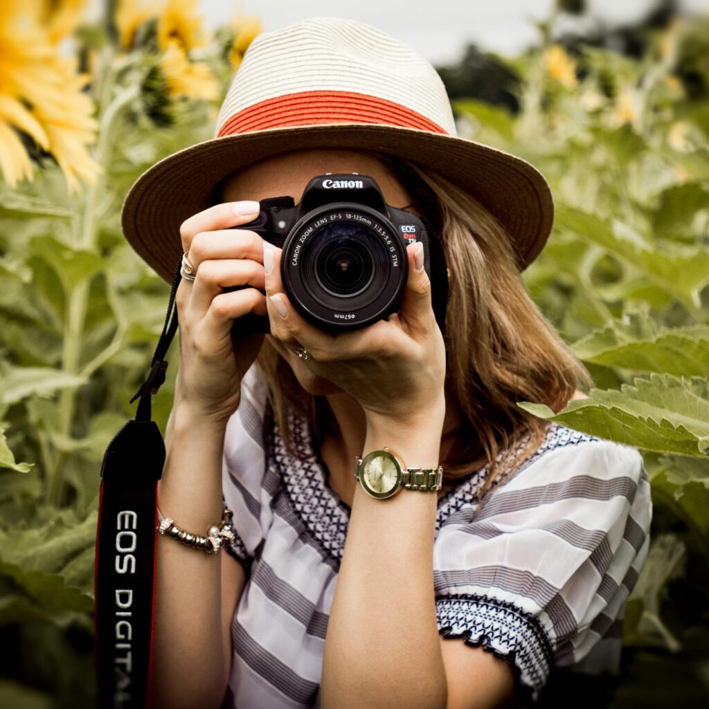 Woman with hat photographing sunflowers in a summer field using a Canon camera.