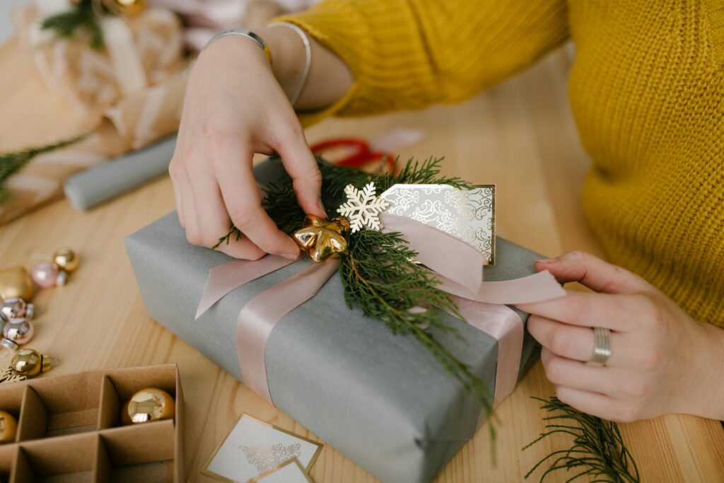 Close-up of hands wrapping a Christmas gift with ribbon and festive decorations.