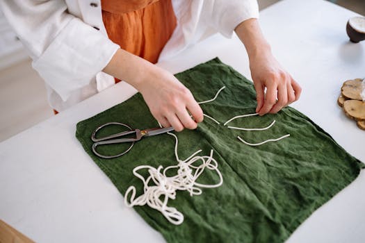 Close-up of hands cutting and arranging candle wicks on green fabric with scissors on a table.
