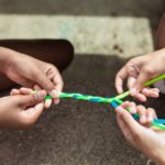 Close-up of kids making vibrant yarn bracelets at summer camp, focusing on hands and creativity.